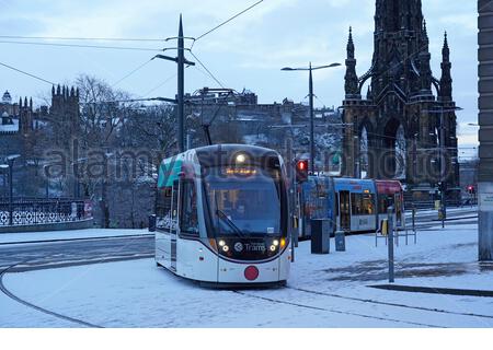 Edinburgh, Schottland, Großbritannien. Januar 2021. Schnee fällt kurz vor Sonnenaufgang im Stadtzentrum. Die Straßenbahn fährt entlang der Princes Street. Kredit: Craig Brown/Alamy Live Nachrichten Stockfoto