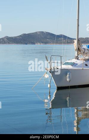 Kleines weißes Segelboot in der Adria mit der Reflexion auf der Wasseroberfläche verankert, Insel Pasman im Hintergrund, Zadar County, Kroatien Stockfoto