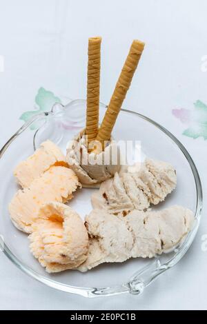 Handgemachtes Eis mit Waffeln auf weißem Hintergrund. Vertikal. Mandarine-Eis und Banana-Rum-Rosinen-Eis. Frisches Hintergrundkonzept, Sommer Stockfoto
