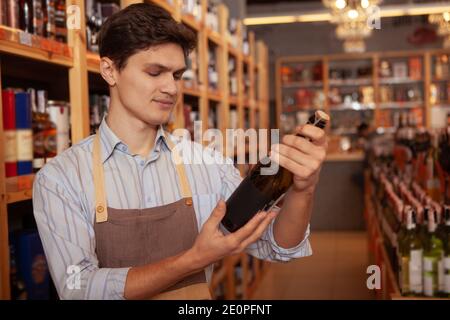Schöner junger männlicher Winzer trägt Schürze, hält Flasche Wein, Kopie Raum Stockfoto