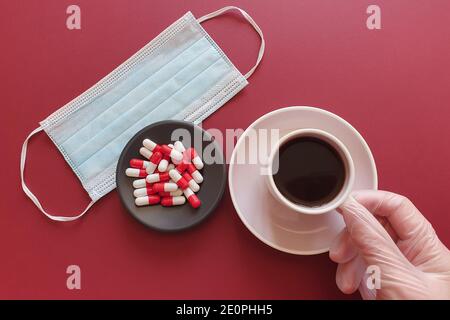 Hand in einem medizinischen Handschuh hält eine Tasse. Schwarzer Kaffee, medizinische Maske und Medikamente. Biologisches Konzept des Lebens. Lifestyle und Flat Lay. Stockfoto