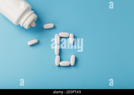 Weiße Kapseln mit Vitaminen in Form von C werden aus einem Glas auf blauem Hintergrund gegossen. Freier Speicherplatz Stockfoto