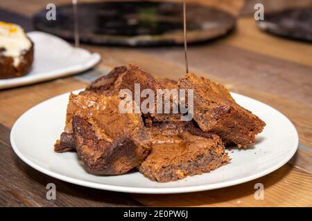Ein Teller mit leckeren Schokolade Brownies auf einer hölzernen Küche Arbeitsplatte, leckere Desserts in einem Haufen bereit, gegessen werden Stockfoto