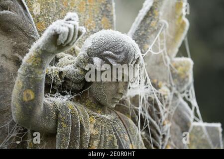 Ein geschnitzter Steinengel in einem mit Frost und Spinnweben bedeckten Garten der Erinnerung nach einer Nacht eisiger Temperaturen am Neujahrstag 2021. Stockfoto