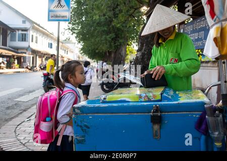 Luang Prabang, Laos - 16. November 2017: Ein unidentifiziertes Schulmädchen, das Eis beim Straßenhändler in Luang Prabang, Laos, kauft. Stockfoto