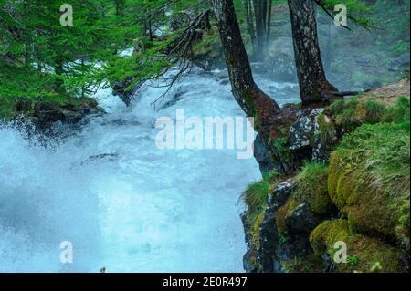 Ein Wasserfall im Tal eines Flusses in den Hautes-Alpes in Frankreich. Die Wirbel verursachen eine Wolke aus blendend weißem Nebel. Am Ufer wachsen Flecken von Gras. Stockfoto