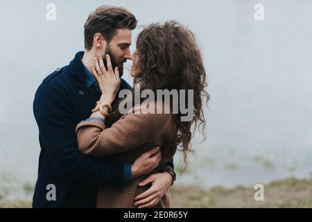 Glückliche Liebhaber in der Nähe des Sees. Das junge Paar umarmt sich am Herbsttag im Freien. Ein bärtiger Mann und eine lockige Frau in der Liebe. Valentinstag. Konzept der Liebe ein Stockfoto