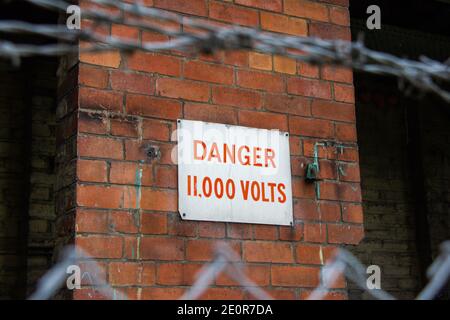 Gefahr 11,000 Volt Schild an Ziegelwand. Hochspannung Stockfoto