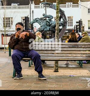 London Großbritannien, Januar 02 2021, älterer schwarzer Mann, der alleine sitzt und auf EINEM Mobiltelefon spricht, draußen auf EINER hölzernen Sitzbank Stockfoto