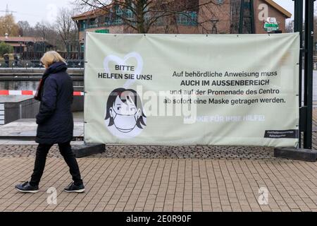 Centro, Oberhausen, NRW, Deutschland. Januar 2021. Eine Frau geht an einem Banner vorbei, das die Menschen an eine obligatorische Maske innerhalb und außerhalb des Einkaufszentrums erinnert, wo Tausende normalerweise mit Einkaufstaschen beladen spazieren würden. Deutschlands größtes Einkaufszentrum und die umliegenden Restaurants, Cafés und Unterhaltungsangebote wirken düster und menschenleer, die Eingänge sind abgesperrt und geschlossen. Das beliebte Einkaufszentrum mit 125.000 m² Gewerbefläche und der gesamten Außenfläche würde normalerweise mit Käufern auf der Suche nach Schnäppchen in den Januar-Verkäufe hallten. Kredit: Imageplotter/Alamy Live Nachrichten Stockfoto