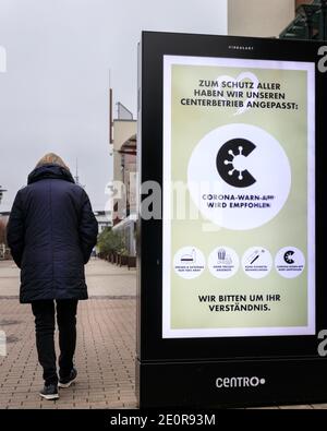 Centro, Oberhausen, NRW, Deutschland. Januar 2021. Eine Frau geht an einem Banner vorbei, das die Verwendung der Corona Warning App und sozialer Distanzierungsregeln rät. Deutschlands größtes Einkaufszentrum und die umliegenden Restaurants, Cafés und Unterhaltungsangebote wirken düster und menschenleer, die Eingänge sind abgesperrt und geschlossen. Das beliebte Einkaufszentrum mit 125.000 m² Gewerbefläche und der gesamten Außenfläche würde normalerweise mit Käufern auf der Suche nach Schnäppchen in den Januar-Verkäufe hallten. Kredit: Imageplotter/Alamy Live Nachrichten Stockfoto