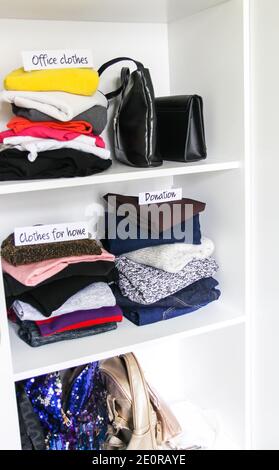 Kleidung und Accessoires Sortierung in der Garderobe auf weißem Regal Hintergrund. Bürokleidung, Kleidung für zu Hause, Spendenpapier Notizen Stockfoto