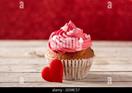 Cupcake dekoriert mit Zuckerherzen zum Valentinstag auf Holz Tabelle und roter Hintergrund Stockfoto