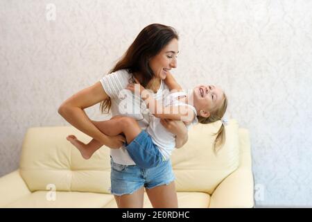 Fröhlich glücklich junge Erwachsene Mutter lachen Spaß mit niedlichen kleinen Kind Tochter spielen, lustige Eltern Mutter halten umarmt kleine Vorschule Kind Stockfoto