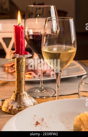 Weißweinglas mit Rotweinglas auf rustikaler Trattoria Tischset mit roter Kerze in goldenem Messingleuchter Stockfoto