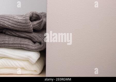 Ein Stapel Wollpullover auf dem Regal. Pullover in Grau und Weiß. Warm und gemütlich. Strickmode. Stockfoto