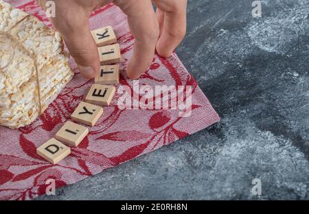 Männliche Hand Befestigung Holzbuchstabe neben leckeren Knäckebrot Stockfoto