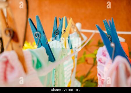 Blau und gelb Holz und Kunststoff Wäscheklammern hält Kleidung in der Sonne auf einer Wäscheleine Trocknen nach dem Waschen. Selektiver Fokus. Terrakotta-Backgroun Stockfoto