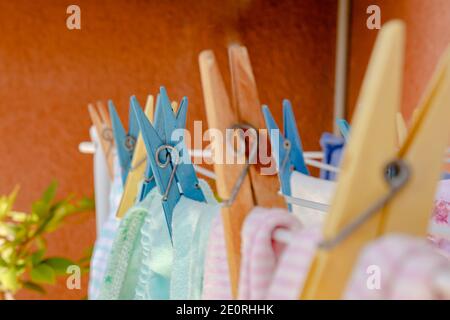 Blau und gelb Holz und Kunststoff Wäscheklammern hält Kleidung in der Sonne auf einer Wäscheleine Trocknen nach dem Waschen. Selektiver Fokus. Terrakotta-Backgroun Stockfoto