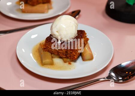 Ein Teller mit traditionellem Parkin mit yorkshire Rhabarber und Eis Creme auf einem hölzernen Hintergrund in einer Küche Stockfoto