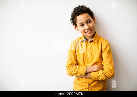 Cute positive kleine lockiges Haar Junge stehen bei der weißen Wand Stockfoto