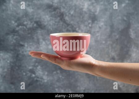 Weibliche Hand hält eine rosa Schale auf einem grauen Hintergrund Stockfoto