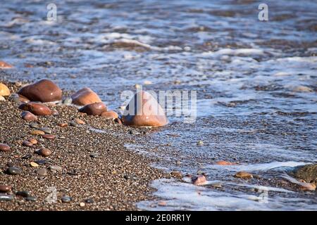 Felsen am Ufer des Strandes, unfokussierter Hintergrund, niemand, Nahaufnahme, sonnig, große und kleine Steine Stockfoto