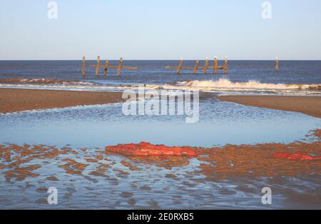 Ein Blick auf einen Gezeitenpool mit Mauerwerksresten und alten Seeverteidigungsstellen am Strand bei Niedrigwasser in Happisburgh, Norfolk, England, Großbritannien. Stockfoto