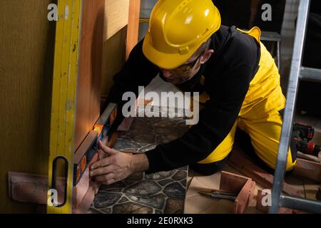 Beim Verlegen der dekorativen Ziegel muss man mit der Wasserwaage von Zeit zu Zeit prüfen, ob die vertikalen und horizontalen richtig sind. Ein Mitarbeiter, der persönliche Schutzausrüstung trägt. Stockfoto