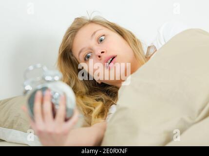 Frau im Bett sah schockiert auf ihren Wecker Stockfoto