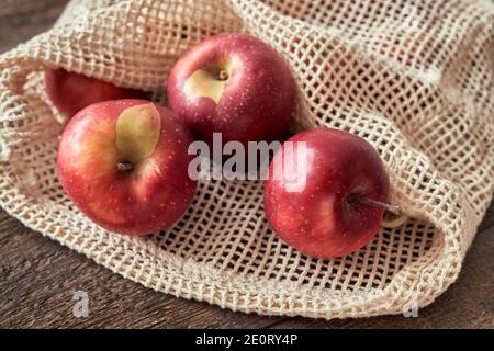 Hässliche Äpfel in einem ökologischen wiederverwendbaren Netzbeutel aus Bio-Baumwolle auf einem Holztisch Stockfoto