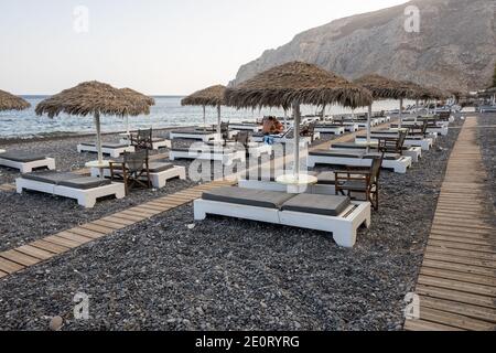 Santorini, Griechenland - 18. September 2020: Sonnenliegen am schwarzen vulkanischen Sandstrand von Kamari in Santorini. Kykladen, Griechenland Stockfoto