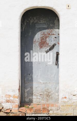 Geschlossene graue Stahltür in einer alten weißen Steinwand, vertikale Hintergrund Foto Textur Stockfoto