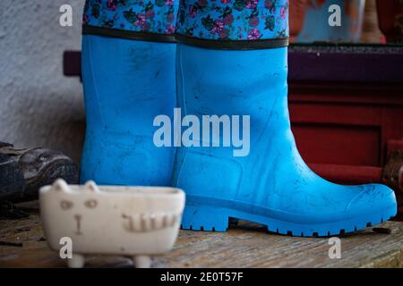 Alte schmutzige Gummistiefel stehen auf dem Holzboden einer Landhausveranda. Blaue Gummi Land Goloshes. Irland Stockfoto