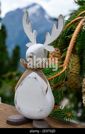 Grüner Weihnachtsbaum mit Zapfen wächst in Französisch Alpen Berge, lustige Holzspielzeug weihnachtselch Nahaufnahme und Gipfel im Hintergrund Stockfoto