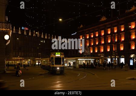 Paradeplatz in der weihnachtszeit bei Nacht. Beleuchtete Fenster des Hauptquartiers von Banken und Straßenbahnhaltestelle in Zürich mit vielen Hängelampen namens Lucy. Zur Stockfoto