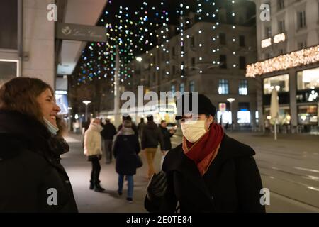 Zwei Frauen mit Maske reden und lachen in der berühmten bahnhofstraße zur Weihnachtszeit. Beleuchtete hängende diamantene Lichter im Hintergrund. Z Stockfoto