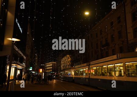 Bahnhofstrasse zur Weihnachtszeit in der Zeit des Corona-Virus. Viele Hängelampen genannt Lucy, Fußgänger und Straßenbahn am Abend. Zürich, 19. Dezember 2020 Stockfoto