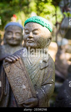 Statuen der ursprünglichen Anhänger Buddhas (Shaka Nyorai in Japan" genannt), mit gestrickten Mützen an Daisho-in Tempel (Daishoin Tempel), Miyajima, Japan. Stockfoto