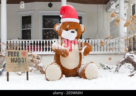 Ein Weihnachtshof mit einem großen Teddybär Werbung Kostenlose Umarmungen während der Covid-19 Pandemie von 2020 Stockfoto