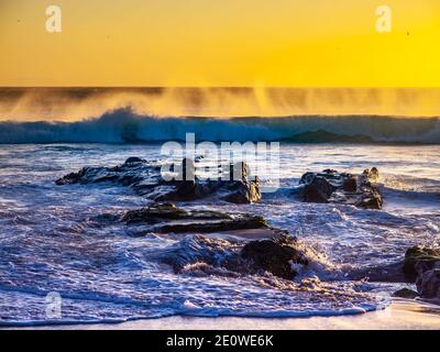 Wellen, die während EINES Sturms am Strand bei Sonnenuntergang auf die Felsen krachen, Costa De La Luz Stockfoto