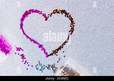 Herzform aus mehrfarbigem Glitzer. Zwei Sektgläser mit herzförmigem Konfetti auf ultimativem grauen Glitzer-Hintergrund. Valentinstag Stockfoto