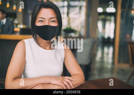 Asiatische reife Geschäftsfrau trägt schützende Gesichtsmaske für Coronavirus-Prävention in Innenräumen öffentlichen Raum als Arbeitsbüro, Restaurant, Café Stockfoto