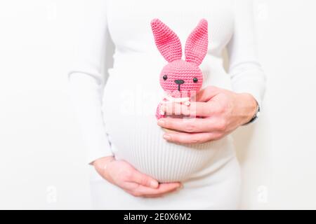 Schwangere Frau im weißen Kleid hält niedlichen Spielzeug Hase. Zukünftige Mutter in Erwartung des Babys. Konzept der Schwangerschaft und Erwartung. Stockfoto