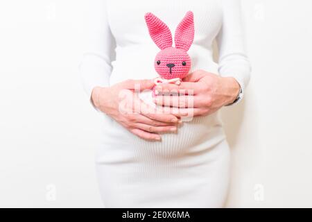 Schwangere Frau im weißen Kleid hält niedlichen Spielzeug Hase. Zukünftige Mutter in Erwartung des Babys. Konzept der Schwangerschaft und Erwartung. Stockfoto