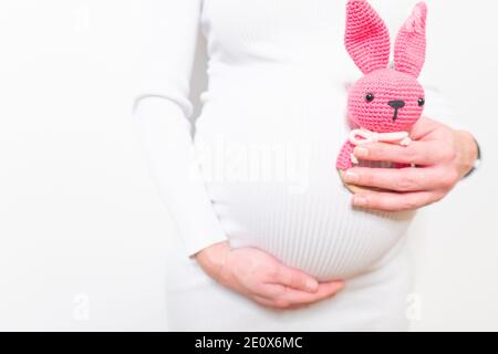 Schwangere Frau im weißen Kleid hält niedlichen Spielzeug Hase. Zukünftige Mutter in Erwartung des Babys. Konzept der Schwangerschaft und Erwartung. Stockfoto