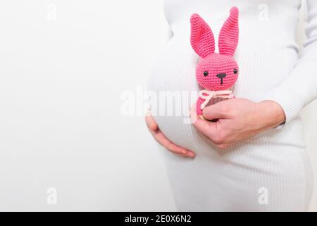 Schwangere Frau im weißen Kleid hält niedlichen Spielzeug Hase. Zukünftige Mutter in Erwartung des Babys. Konzept der Schwangerschaft und Erwartung. Stockfoto