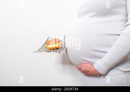 Schwangerschaft und ungesunde Ernährung Konzept: Schwangere Frau hält einen Teller mit leckeren Donuts in der Hand Stockfoto