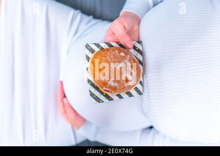 Schwangerschaft und ungesunde Ernährung Konzept: Schwangere Frau hält einen Teller mit leckeren Donuts in der Hand Stockfoto