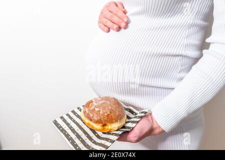 Schwangerschaft und ungesunde Ernährung Konzept: Schwangere Frau hält einen Teller mit leckeren Donuts in der Hand Stockfoto